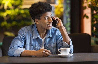 Genç afro adam akıllı telefonda konuşuyor, kenara bakıyor