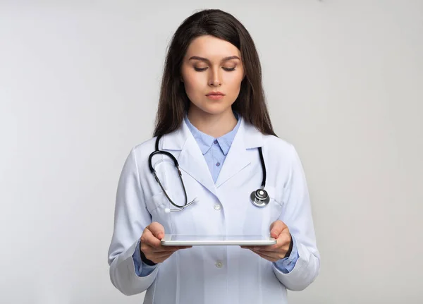 Médico feminino segurando tablet digital em pé sobre fundo branco — Fotografia de Stock