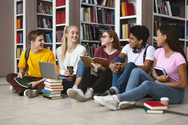 Compañeros sentados en el piso de la biblioteca, charlando mientras estudian — Foto de Stock