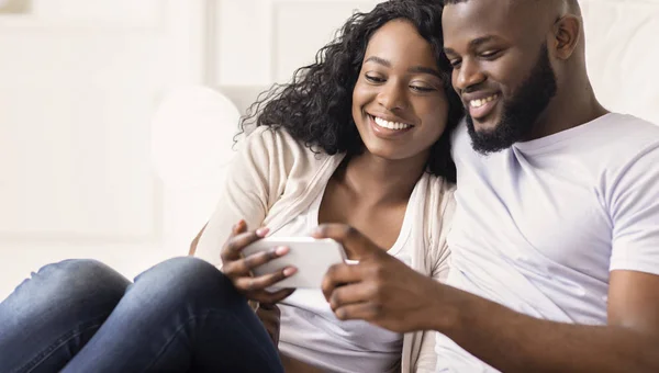 Χαρούμενο αφρικανικό ζευγάρι βλέποντας αστεία βίντεο στο smartphone στο σπίτι — Φωτογραφία Αρχείου