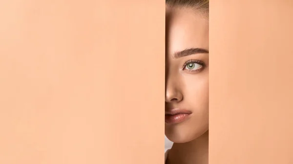 Девушка с обнажённым макияжем заглядывает в дырку в персиковой бумаге — стоковое фото