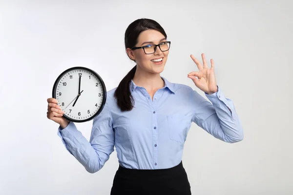 Zakenvrouw Holding klok Gesturing OK op witte studio achtergrond — Stockfoto