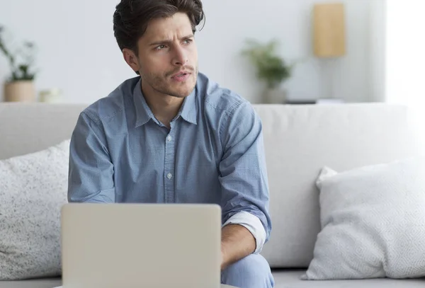 Σκεπτικός επιχειρηματίας στο laptop σκέψης κάθεται στον καναπέ — Φωτογραφία Αρχείου