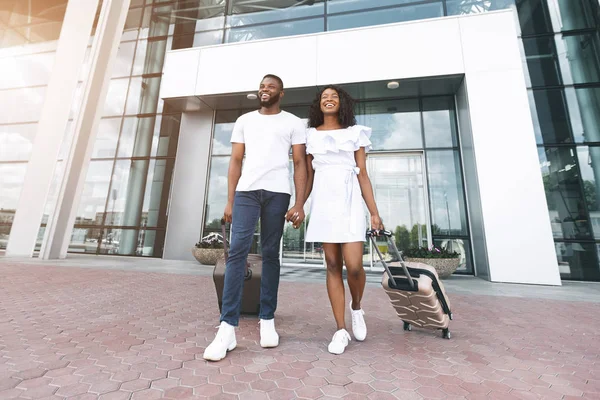 Feliz pareja negra yendo con el equipaje fuera del edificio del aeropuerto — Foto de Stock