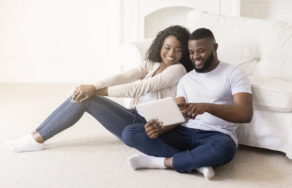 Alegre pareja usando tableta digital juntos mientras están sentados en casa —  Fotos de Stock