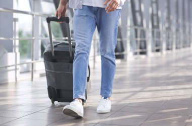 Havaalanı koridorunda bavulla yürüyen adam