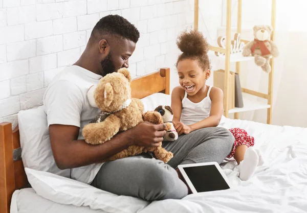 Alegre afro chica jugando juguetes con su papá, sentado en la cama — Foto de Stock