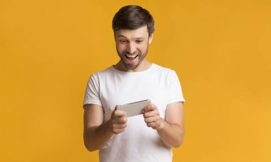 Heyecanlı Adam Sarı Arka Plan Üzerinde Akıllı Telefon Oyunları Oynuyor