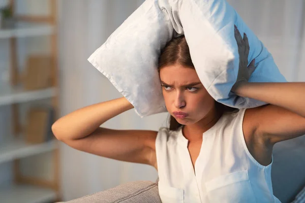 Роздратована жінка покриває голову подушкою страждає від шуму в приміщенні — стокове фото