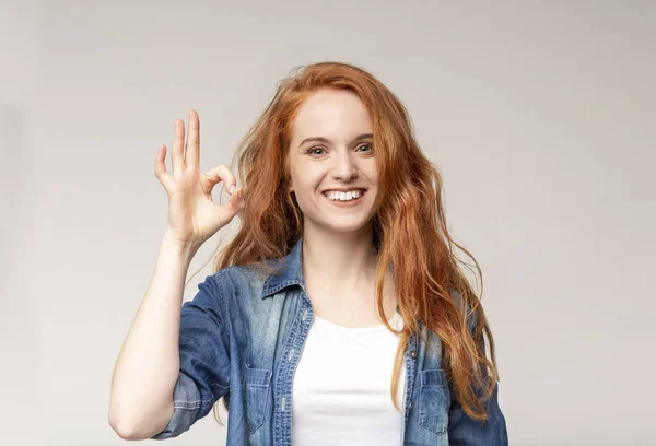 Olumlu kızıl saçlı kız ok işareti gösteren ve kameraya gülümseyen — Stok fotoğraf