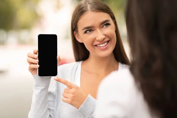 Mujer alegre mostrando a su amigo en blanco pantalla del teléfono inteligente — Foto de Stock