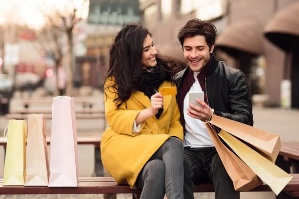 Pareja joven sentada en el banco después de ir de compras —  Fotos de Stock