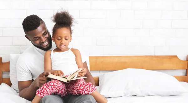 Padre africano leyendo con su adorable hijita en casa — Foto de Stock