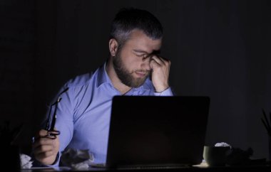 Karanlıkta dizüstü bilgisayarla çalışan, gözlerine dokunan yorgun işadamı