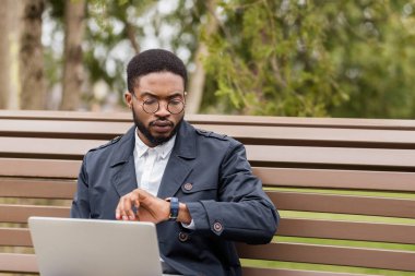 Dizüstü bilgisayar üzerinde çalışan serbest adam açık havada ve zaman kontrol