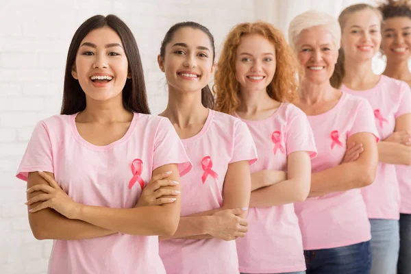 Mujeres con camisetas de cáncer de mama de pie junto a la pared blanca — Foto de Stock