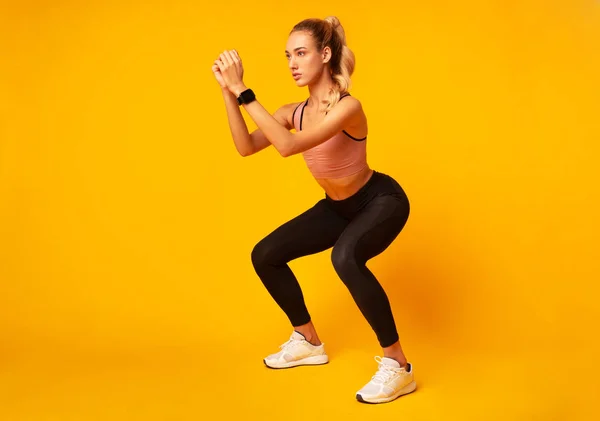 黄色の背景の上に深いスクワット運動をしている若い女性 — ストック写真