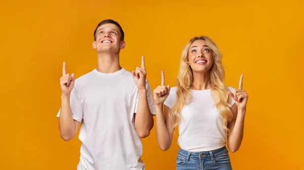 Pareja mirando hacia arriba y apuntando al copyspace sobre fondo amarillo — Foto de Stock