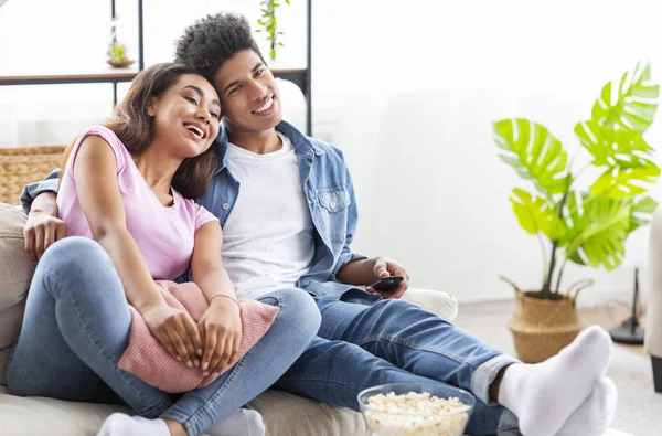 Teenage couple watching tv, sitting on couch with popcorn