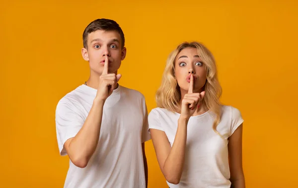 Pareja joven sosteniendo los dedos en los labios y mirando a la cámara — Foto de Stock