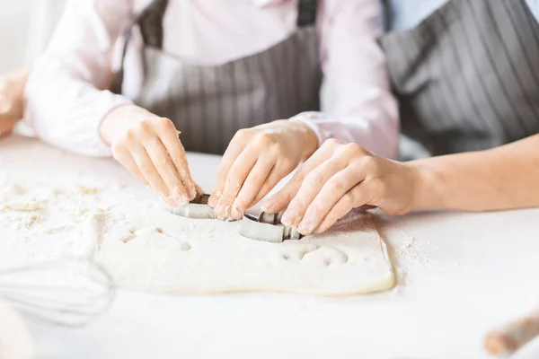 Mother and daughter cutting out different cookie shapes of dough