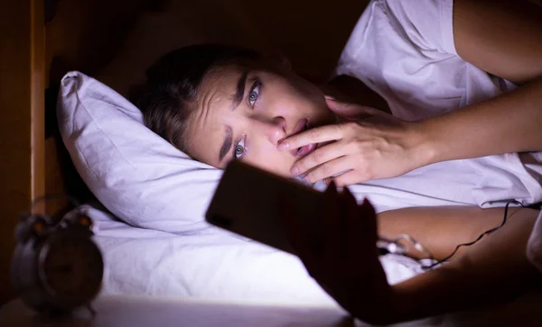 Menina ansiosa usando celular deitado na cama à noite — Fotografia de Stock