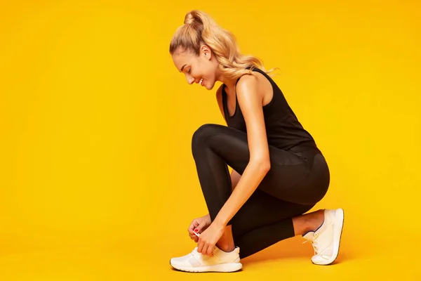 Felice donna allacciatura scarpe prima di allenamento su sfondo giallo — Foto Stock