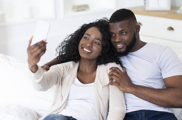 Romantic couple taking selfie while sitting on sofa at home