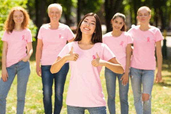 소녀 몸짓 엄지 손가락- 앞 유방암 자원 봉사 그룹 야외 — 스톡 사진