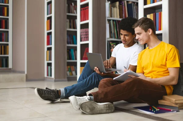 Dois amigos fazendo trabalhos de casa no chão na biblioteca do campus — Fotografia de Stock