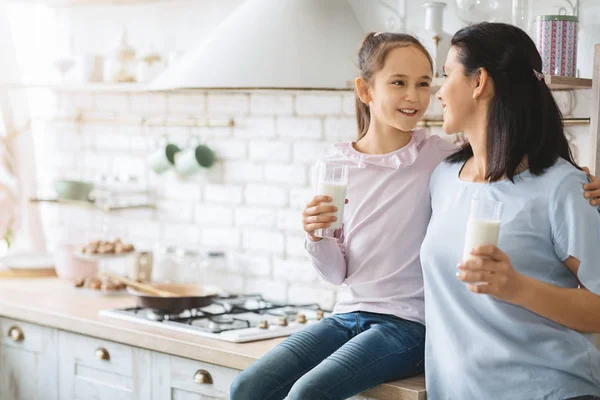 Mãe e filha felizes bebendo leite e sorrindo na cozinha — Fotografia de Stock