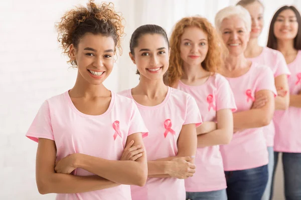 Freiwillige Frauen in Brustkrebs-T-Shirts stehen über der weißen Wand — Stockfoto