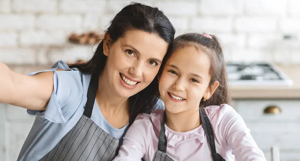 Красивая мама и ее милая дочь делают селфи на кухне — стоковое фото