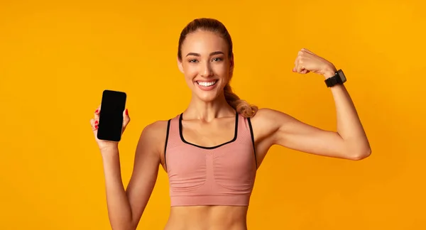 Muchacha sosteniendo Smartphone mostrando músculos sobre fondo amarillo, Mockup, Panorama — Foto de Stock