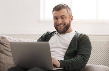 Gülümseyen adam evde dizüstü bilgisayar online çalışan