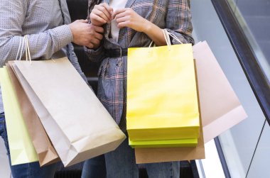 Alışveriş merkezinde yürüyen merdivenle inen kağıt torbalı çift