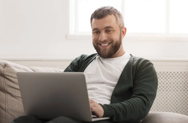 Sonriente hombre trabajando en el ordenador portátil en línea en casa — Foto de Stock