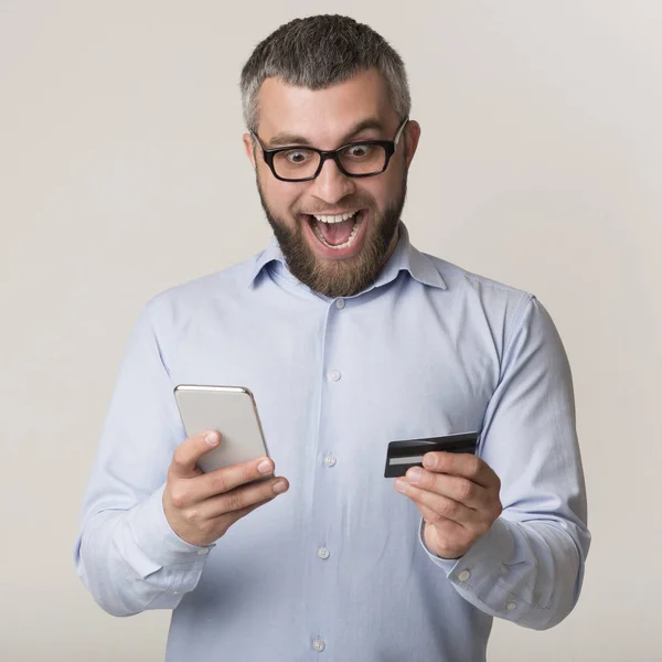 Vzrušený muž držící kreditní kartu, používající mobilní telefon pro nakupování online — Stock fotografie