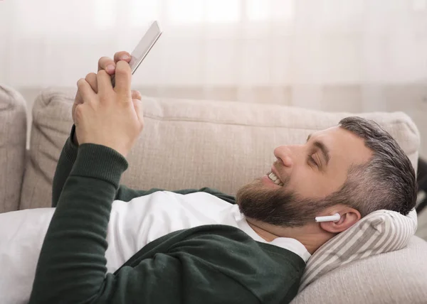 무선 이어폰으로 디지털 태블릿에서 영화를 보는 쾌활한 남자 — 스톡 사진