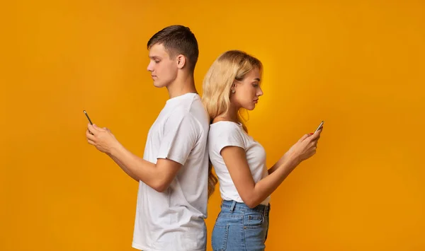Young guy and girl standing back to back with smartphones