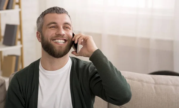 Homem falando no celular em casa e sorrindo — Fotografia de Stock