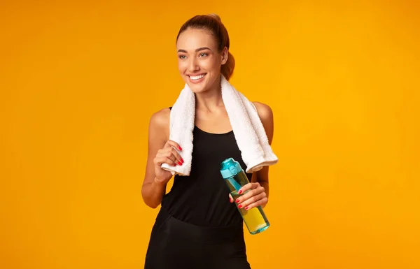 Joven mujer de pie sosteniendo botella de agua y toalla, fondo amarillo — Foto de Stock