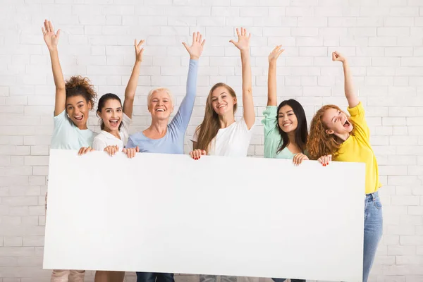 Щасливі різні жінки проведення порожній білої дошки проти білої стіни — стокове фото