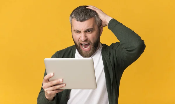 Naštvaný vousatý muž držící tablet, křičel a dotýkal se jeho hlavy — Stock fotografie