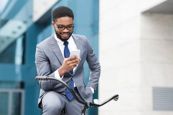 Empresário afro feliz usando smartphone, andando de bicicleta — Fotografia de Stock