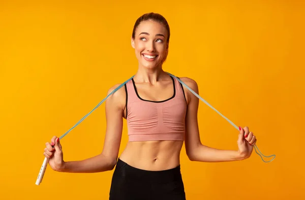 Schlankes Mädchen mit Springseil über gelbem Hintergrund — Stockfoto