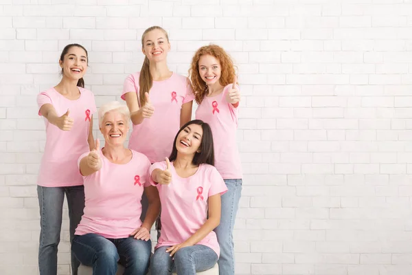 Voluntarios en Camisetas de Cáncer de Mama Gestionando Pulgares Sobre la Pared Blanca — Foto de Stock