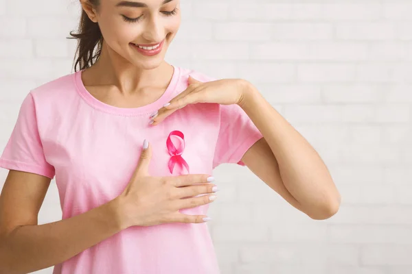 Ragazza che incornicia il nastro rosa sulla maglietta in piedi contro il muro bianco — Foto Stock