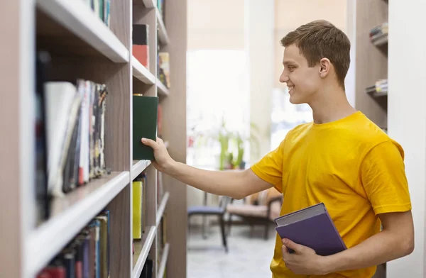 Przystojny młody człowiek wybiera książki w księgarni — Zdjęcie stockowe