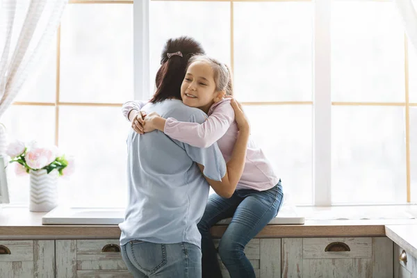 Mujer y su hija abrazándose tiernamente cerca de la ventana en la cocina —  Fotos de Stock